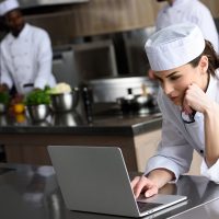 attractive chef using laptop at restaurant kitchen